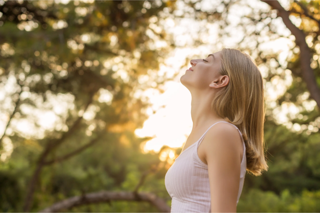 Femme respirant avec sourire en pleine nature, grâce aux bienfaits de la sophrologie à Lyon